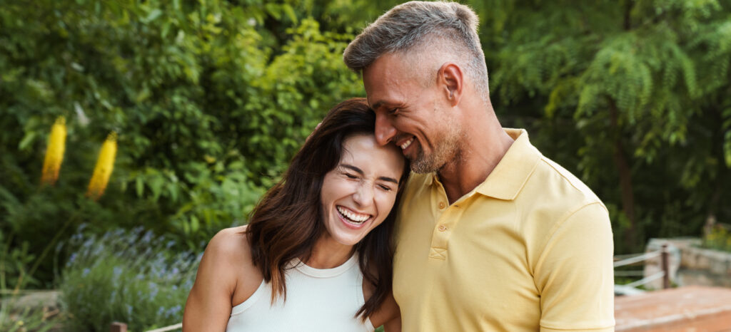 portrait of joyful middle aged couple aughing and hugging while walking in summer park