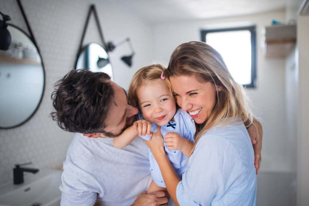 young family with small daughter indoors in bathroom, hugging.