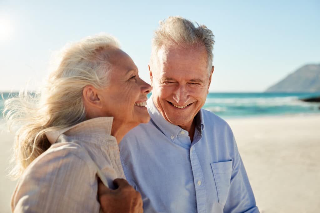 senior white couple walking on a sunny beach, waist up, side view, close up