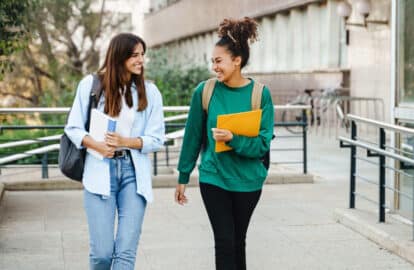 two happy students walking and talking each other in university campus after classes