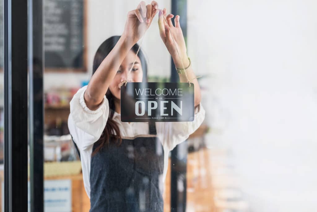 back view glass door small business owner holding a sign to open